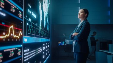 Genç Kadın Bilgisayar Bilimi Mühendisi Büyük Ekran 'a bakıyor ve Veri Göstergeleriyle Küresel Haritayı gösteriyor. Sunucularla Telekomünikasyon Teknolojisi Sistem Kontrolü ve İzleme Odası.