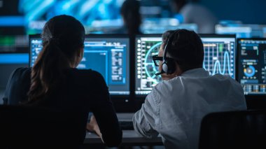 Büyük Dijital Ekrandaki Küresel Haritadan Canlı Ananliz Kaynağı ile İki Uzman Çalışması. Çalışanlar, Finansal Borsa Ticareti Bilgileri ve Büyük Verilerle Ekranların Önünde Oturuyorlar.