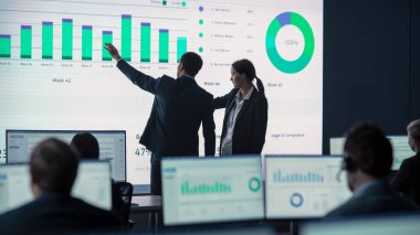 İki Tüccar, Modern İzleme Ofisinde Büyük Dijital Ekranla Analitik Kaynak Yapıyor. Komisyoncular ve Finans Uzmanlarıyla İzleme Odası Bilgisayarların Önünde Oturuyor. Meslektaşlar Konuşur.