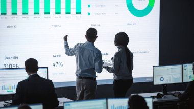 İki Tüccar, Modern İzleme Ofisinde Büyük Dijital Ekranla Analitik Kaynak Yapıyor. Komisyoncular ve Finans Uzmanlarıyla İzleme Odası Bilgisayarların Önünde Oturuyor. Meslektaşlar Konuşur.