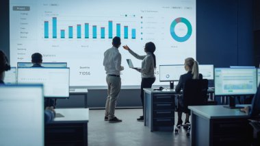İki Tüccar, Modern İzleme Ofisinde Büyük Dijital Ekranla Analitik Kaynak Yapıyor. Komisyoncular ve Finans Uzmanlarıyla İzleme Odası Bilgisayarların Önünde Oturuyor. Meslektaşlar Konuşur.