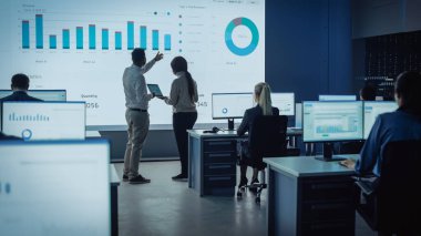 İki Tüccar, Modern İzleme Ofisinde Büyük Dijital Ekranla Analitik Kaynak Yapıyor. Komisyoncular ve Finans Uzmanlarıyla İzleme Odası Bilgisayarların Önünde Oturuyor. Meslektaşlar Konuşur.