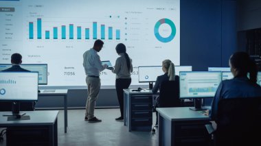 İki Tüccar, Modern İzleme Ofisinde Büyük Dijital Ekranla Analitik Kaynak Yapıyor. Komisyoncular ve Finans Uzmanlarıyla İzleme Odası Bilgisayarların Önünde Oturuyor. Meslektaşlar Konuşur.