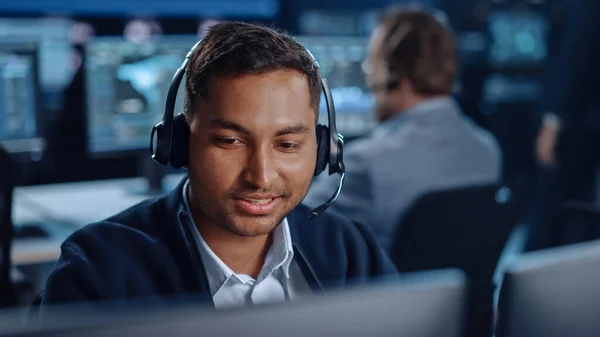 Close Up Portrait of a Joyful Technical Customer Support Specialist Conversando em um fone de ouvido enquanto trabalhava em um computador em uma sala de controle de call center preenchida com telas de exibição de computador e servidores de dados — Fotografia de Stock