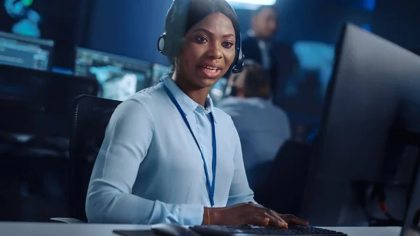 Joyful Beautiful Technical Customer Support Specialist is Talking on a Headset while Working on a Computer in a Call Center Control Room Filled with Colleagues, Display Screens and Data Servers. — Stock Photo, Image