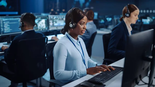 Happy Beautiful Technical Customer Support Specialist está hablando con auriculares mientras trabaja en una computadora en una sala de control de centro de llamadas llena de colegas, pantallas de visualización y servidores de datos. — Foto de Stock