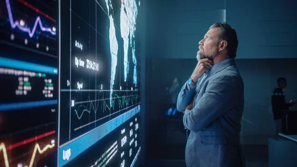 Senior Computer Science Engineer Looking at Big Screen Display Show Global Map with Data Points. Telekomunikační technologie Company System Control and Monitoring Room with Servers. — Stock fotografie