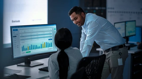 Dos comerciantes profesionales que cuentan y trabajan en una oficina de monitoreo moderna con datos de análisis en vivo en una gran pantalla digital. Sala de monitoreo con corredores y especialistas en finanzas. —  Fotos de Stock