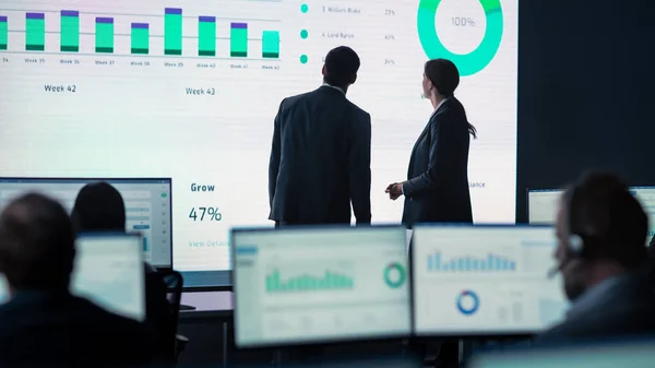 Zwei Händler treffen sich in einem modernen Monitoring-Büro mit Analytik-Feed auf einem großen digitalen Bildschirm. Überwachungsraum mit Maklern und Finanzspezialisten sitzen vor Computern. Kollegen reden. — Stockfoto