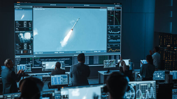 Group of People in Mission Control Center Witness Successful Space Rocket Launch. Flight Control Employees Sit in Front Computer Displays and Monitor the Crewed Mission.