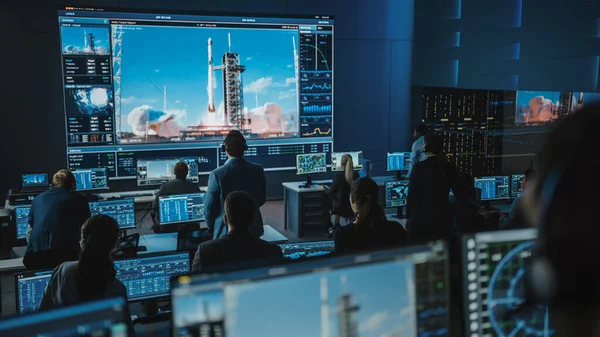 Grupo de Pessoas no Centro de Controle de Missão Testemunha de Sucesso no Lançamento do Foguete Espacial. Funcionários de Controle de Voo Sentam-se em monitores de computador da frente e monitoram a missão tripulada. Equipe Levante-se e Assista. — Fotografia de Stock