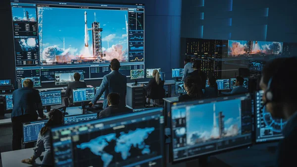 Grupo de Pessoas no Centro de Controle de Missão Testemunha de Sucesso no Lançamento do Foguete Espacial. Funcionários de Controle de Voo Sentam-se em monitores de computador da frente e monitoram a missão tripulada. Equipe Levante-se e Assista. — Fotografia de Stock