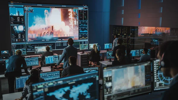 Grupo de personas en el Centro de Control de Misión son testigos del lanzamiento exitoso de cohetes espaciales. Los empleados de Control de Vuelo se sientan en las pantallas delanteras de la computadora y monitorean la misión tripulada. Equipo de pie y ver. —  Fotos de Stock