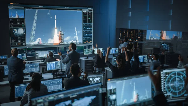 Група людей в Центрі управління польотами Усвідомлення успішного запуску космічних ракет. Працівники управління польотами сидять на передніх комп'ютерних виставках і контролюють пілотовану місію. Команда встає і клацає руки. — стокове фото