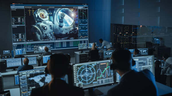 Group of People in Mission Control Center Establish Successful Video Connection on a Big Screen with an Astronaut on Board of a Space Station. Flight Control Scientists Sit in Front Computer Displays.