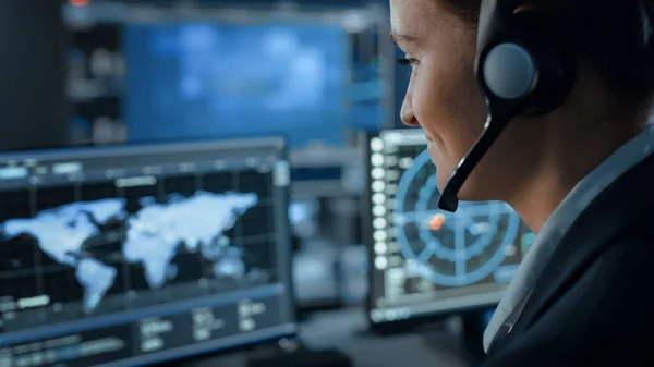 Computerskærm med Global Map Technology Bruges af en kvindelig flyveleder i et Mission Control Center Room med andre forskere. Team of Engineers Arbejde i overvågningsrummet Fuld af skærme. - Stock-foto