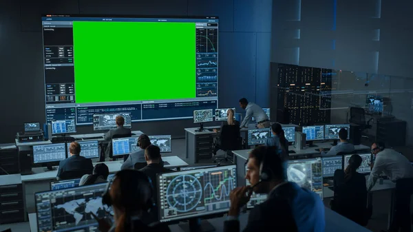 Groot groen scherm Horizontale Mock Up in een Mission Control Center kamer met Flight Director en andere controllers werken aan computers. Team van Ingenieurs werkt in Monitoring Room vol met Displays. — Stockfoto