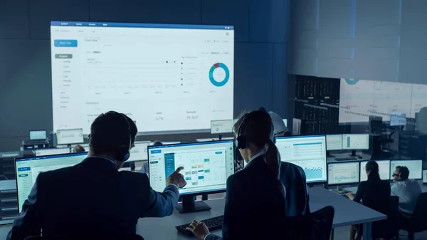 Επαγγελματίες έμποροι που εργάζονται σε ένα σύγχρονο Γραφείο Παρακολούθησης με Live Analytics Feed σε μια μεγάλη ψηφιακή οθόνη. Αίθουσα παρακολούθησης με Brokers and Finance Specialists Καθίστε μπροστά από υπολογιστές. — Φωτογραφία Αρχείου