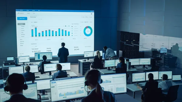 Professionella handlare Arbeta i en modern övervakning kontor med Live Analytics Feed på en stor digital skärm. Övervakningsrum med mäklare och finansspecialister sitter framför datorer. — Stockfoto