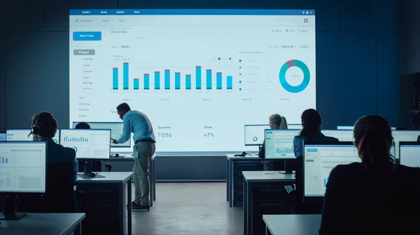 Professionelle Händler arbeiten in einem modernen Überwachungsbüro mit Live-Analytics-Feed auf einem großen digitalen Bildschirm. Überwachungsraum: Makler und Finanzspezialisten sitzen vor Computern. — Stockfoto