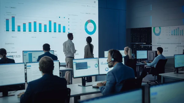 两个交易者在一个现代监控办公室开会，在一个大的数字屏幕上输入分析数据。与经纪人和金融专家一起坐在计算机前的监控室。同事谈心. — 图库照片