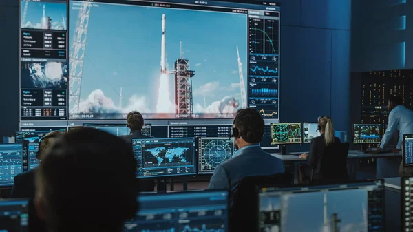 Gruppo di persone nel Centro di Controllo Missione Testimonianza successo lancio razzo spaziale. I dipendenti del controllo di volo siedono nei display del computer anteriore e monitorano la missione con equipaggio. Team Stand Up e battere le mani. — Foto Stock