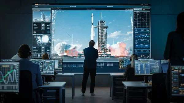 Eine Gruppe von Menschen im Missionskontrollzentrum stellt eine erfolgreiche Videoverbindung auf einem Großbildschirm mit einem Astronauten an Bord einer Raumstation her. Flugkontrolleure sitzen vor Computern. — Stockfoto