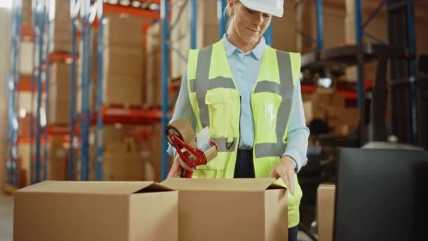 Dans un grand entrepôt, une ouvrière scelle une boîte en carton avec un distributeur de ruban d'étanchéité — Video