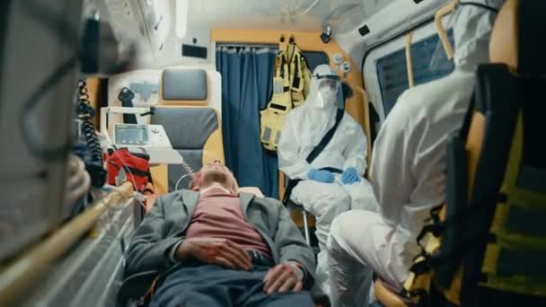 Paramédicos Montar en Coveralls Traje de materiales peligrosos en ambulancia con paciente — Vídeos de Stock