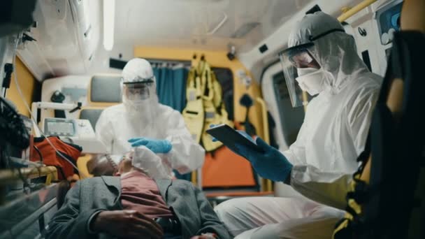 Paramédico en Coveralls Montar en ambulancia usando la tableta con el paciente — Vídeo de stock