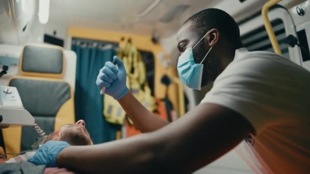 Sanitäter mit Gesichtsmaske untersuchen verletzten Patienten im Rettungswagen — Stockvideo