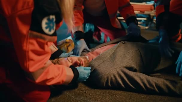 Paramedicinere giver medicinsk hjælp til unge mand liggende på en gade – Stock-video
