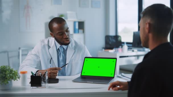 医師が患者に話しかけ、ノートパソコンで緑の画面のモックを使用する — ストック動画
