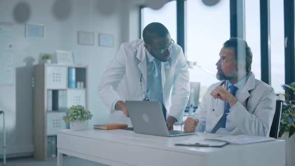 Dos médicos hablan al lado de la computadora en la oficina del hospital — Vídeo de stock