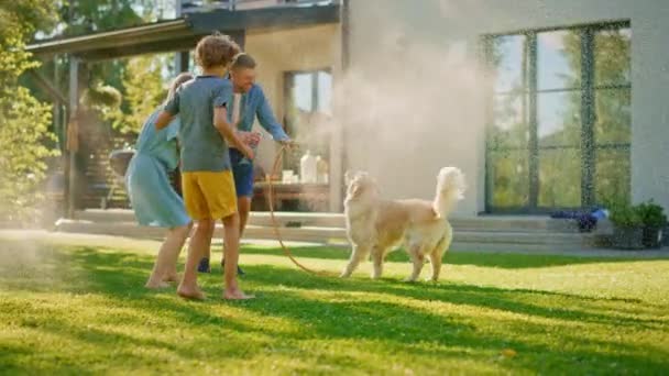 Fader dotter och son leka med slang Golden Retriever hund i trädgården — Stockvideo