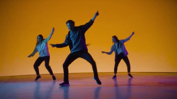 Три танцора выступают перед цветным цифровым экраном — стоковое видео