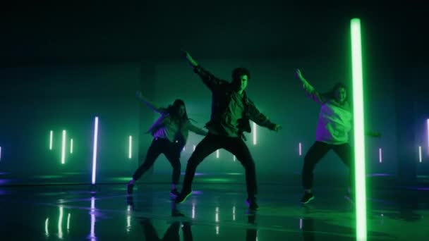 Trzech tancerzy występujących przed cyfrowym neonem ekranu garażu — Wideo stockowe