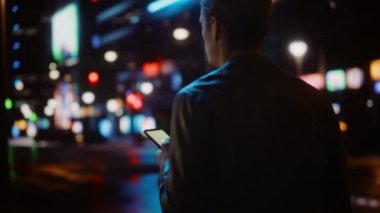Şehir gecesinde akıllı telefon kullanan adam.
