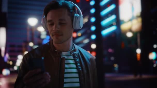 Hombre con auriculares caminando por la ciudad nocturna — Vídeos de Stock