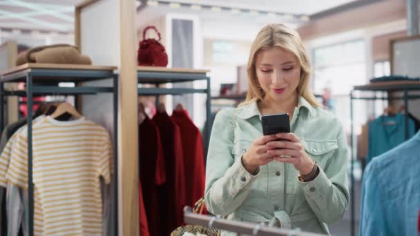 Cliente feminino com smartphone na loja de roupas — Vídeo de Stock