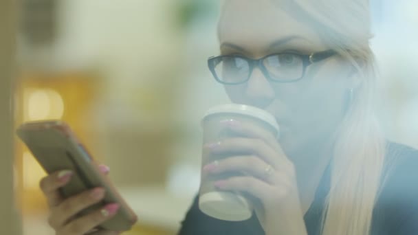 Frau trinkt Kaffee, während sie Handy im Kaffee benutzt — Stockvideo