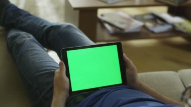 Döşeme evde kanepede ve yeşil ekran manzara modunda tabletiyle nöbette adamdır