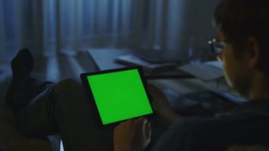 Adam Gece Vakti Kanepede Yatıyor ve Yatay Modda Yeşil Ekranile Tablet Kullanıyor