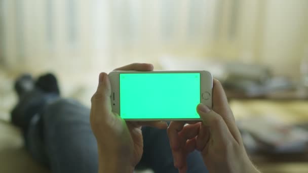 L'homme repose sur le canapé à la maison et utilise le téléphone avec écran vert en mode paysage . — Video