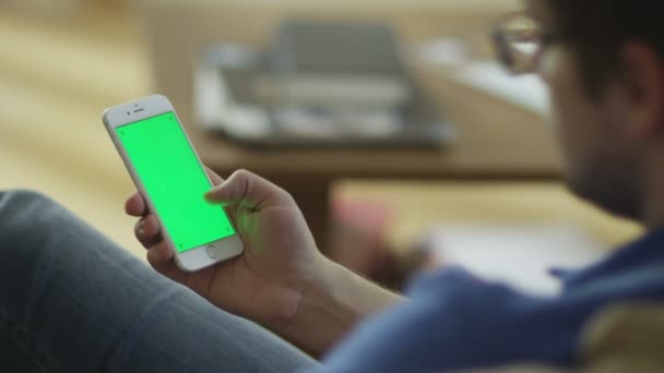 El hombre está usando el teléfono con pantalla verde en modo retrato en casa — Vídeo de stock