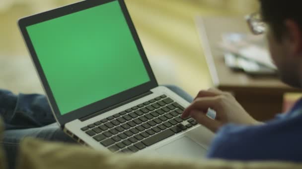 Человек лежит на диване и с помощью ноутбука с зеленым экраном дома — стоковое видео