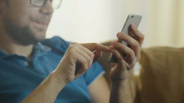 Homem está sentado no sofá e usando telefone celular — Vídeo de Stock