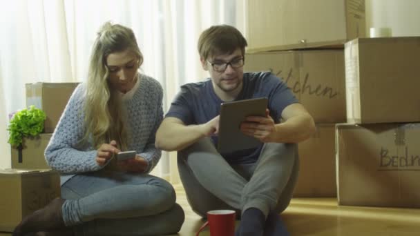 Pareja joven está utilizando el teléfono y la tableta para el entretenimiento en la nueva casa . — Vídeo de stock