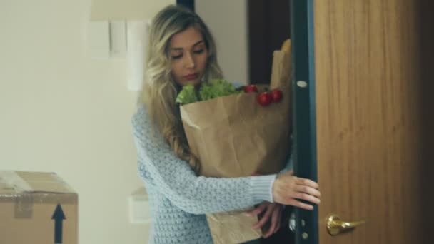 La mujer viene a casa. Bolsa de mano con comida en las manos . — Vídeo de stock