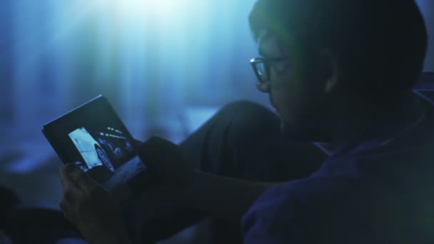 Homem no sofá está assistindo filme de ação no tablet à noite — Vídeo de Stock